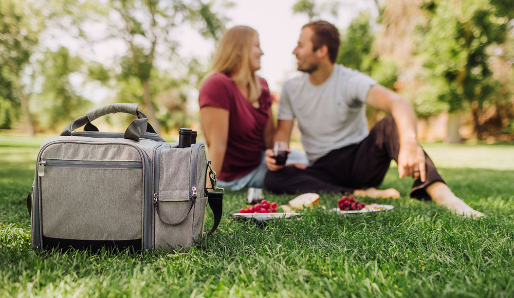 couple sitting on grass having a picnic with insulated picnic cooler bag