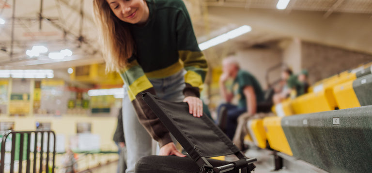 woman setting collapsible stadium seat on the bleachers during a basketball game