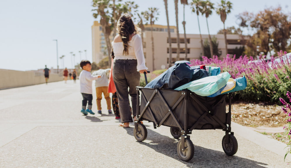 mom pulling wagon full of beach gear down the boardwalk with two small kids running in front of her