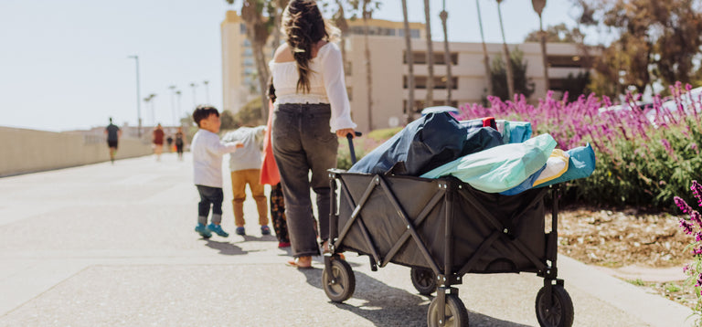 mom pulling wagon full of beach gear down the boardwalk with two small kids running in front of her