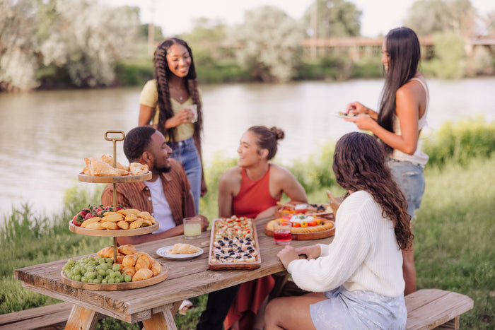 A group of people enjoying a meal together at a picnic table filled with various foods and drinks.