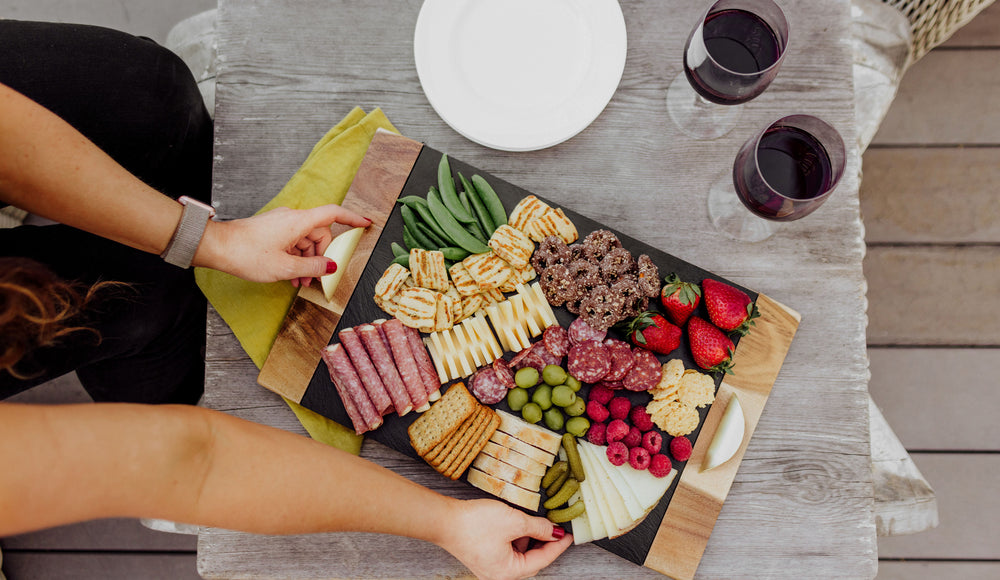 woman placing slate and acacia charcuterie board on the table with two glasses of wine